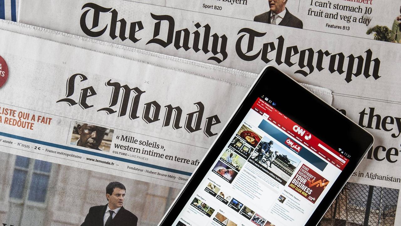 Das Touchscreen eines digitalen Tablets zeigt die CNN International online Nachrichten, welches auf den beiden Zeitungen, der britische "The daily Telegraph" und der französischen "Le monde" liegt.