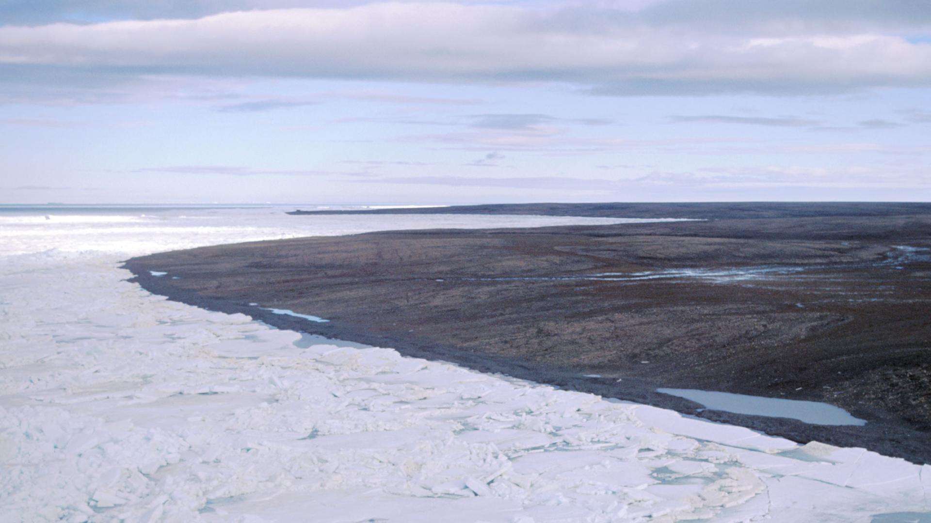 Blick über eine durch Dauerfrost (Permafrost) gezeichnete Landschaft auf der zur Russland gehörenden Bolschewik Insel, während im Vordergrund noch Packeis herrscht ist im Hintergrund die Landschaft schon aufgetaut und schlammig.  