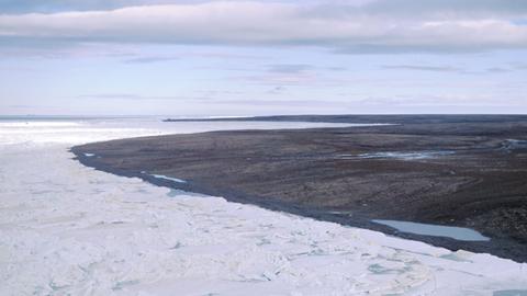 Blick über eine durch Dauerfrost (Permafrost) gezeichnete Landschaft auf der zur Russland gehörenden Bolschewik Insel, während im Vordergrund noch Packeis herrscht ist im Hintergrund die Landschaft schon aufgetaut und schlammig.