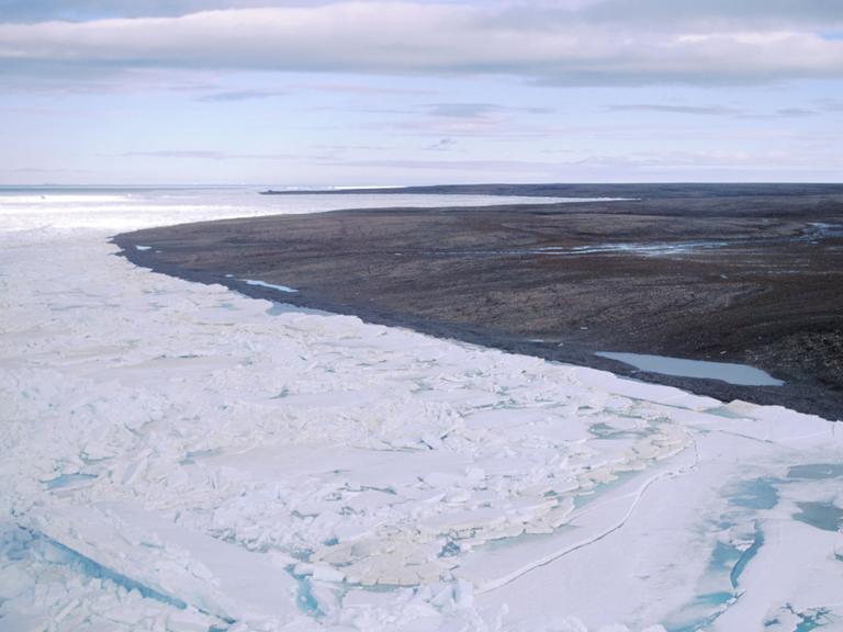 Blick über eine durch Dauerfrost (Permafrost) gezeichnete Landschaft auf der zur Russland gehörenden Bolschewik Insel, während im Vordergrund noch Packeis herrscht ist im Hintergrund die Landschaft schon aufgetaut und schlammig.