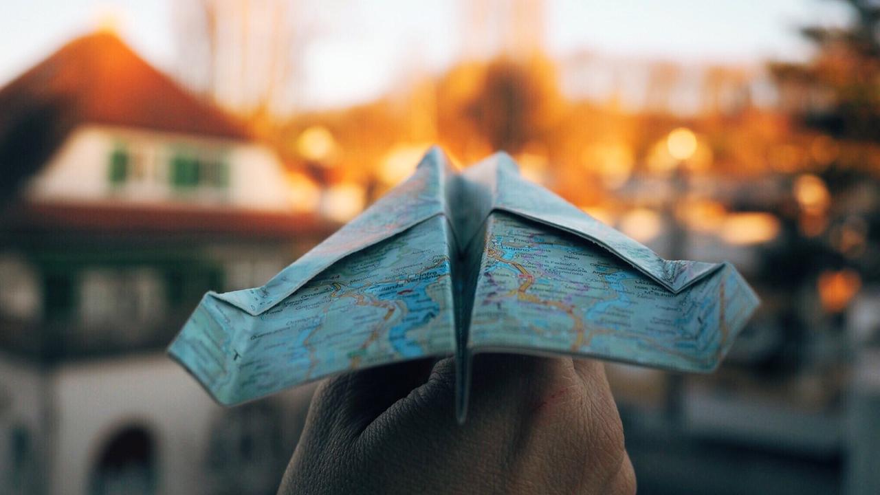 Eine Hand hält einen Papierflieger. aus einer Weltkarte gefaltet