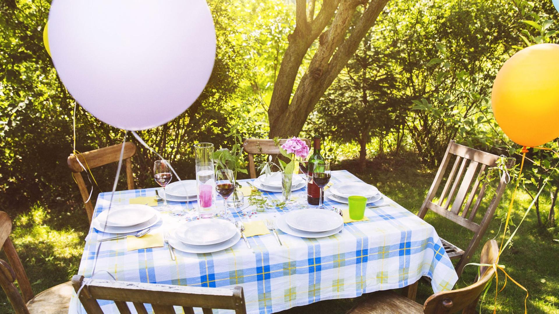 Ein Tisch in einem Garten, an den Stühlen hängen Luftballons.
