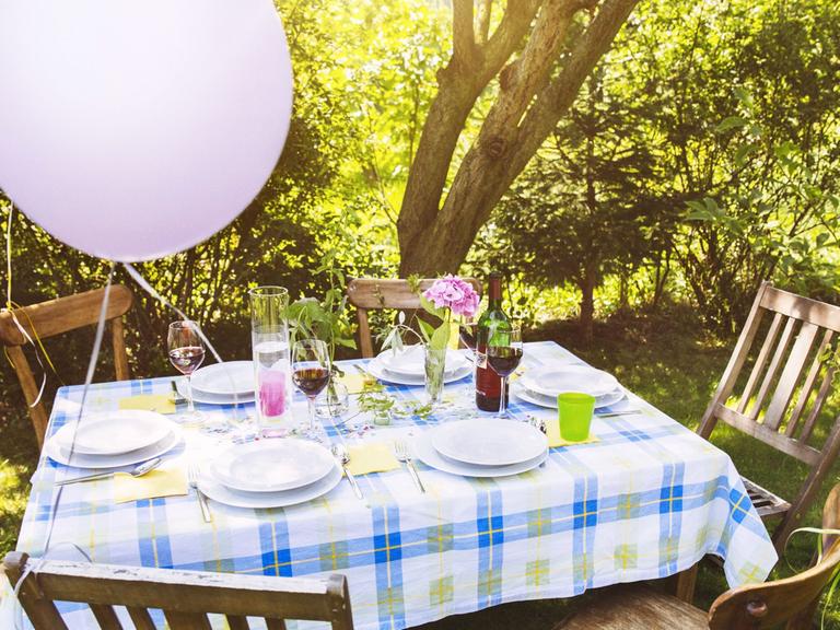 Ein Tisch in einem Garten, an den Stühlen hängen Luftballons.