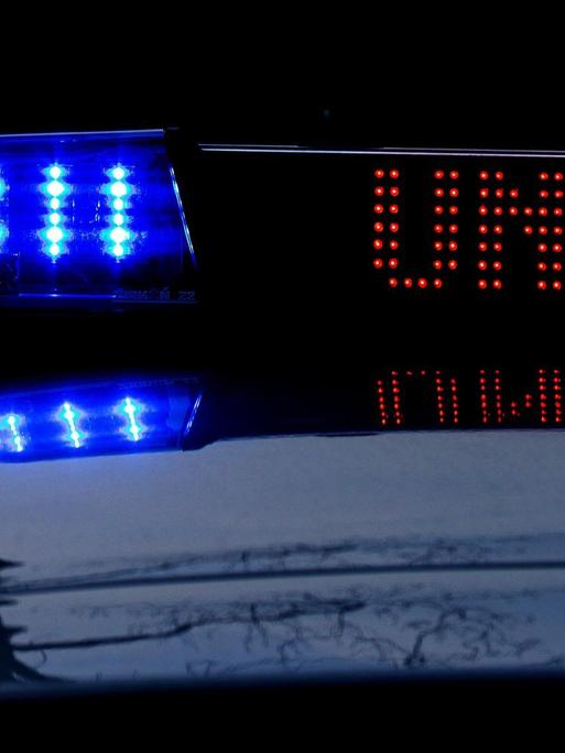 Detailaufnahme eines Einsatzfahrzeugs der Polizei in der Dunkelheit, mit Blaulicht und dem roten Schriftzug "Unfall" im Display.