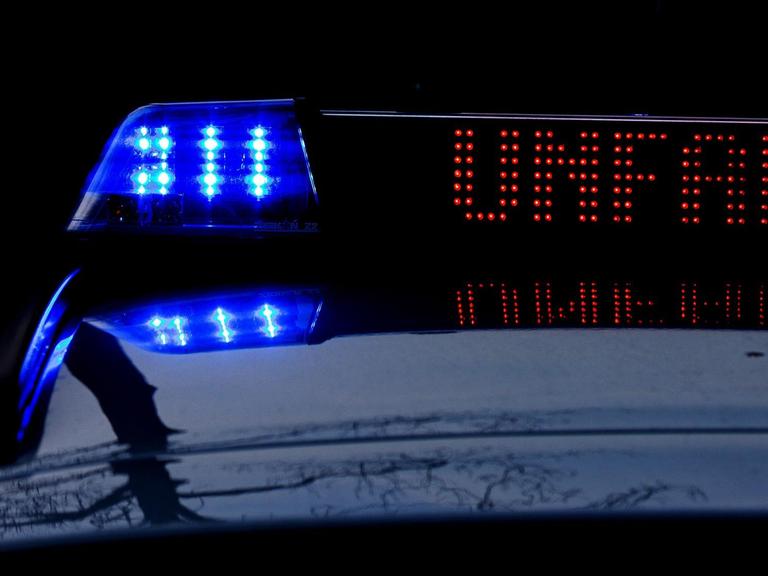 Detailaufnahme eines Einsatzfahrzeugs der Polizei in der Dunkelheit, mit Blaulicht und dem roten Schriftzug "Unfall" im Display.