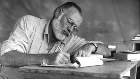 Der amerikanische Schriftsteller Ernest Hemingway sitzt an einem Tisch und schreibt in einen Block in Kenia im September 1952.