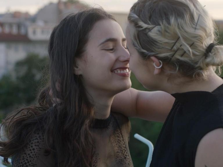 Filmszene aus Yung. Zu sehen sind zwei junge DarstellerInnen auf einem Balkon, die sich küssen.