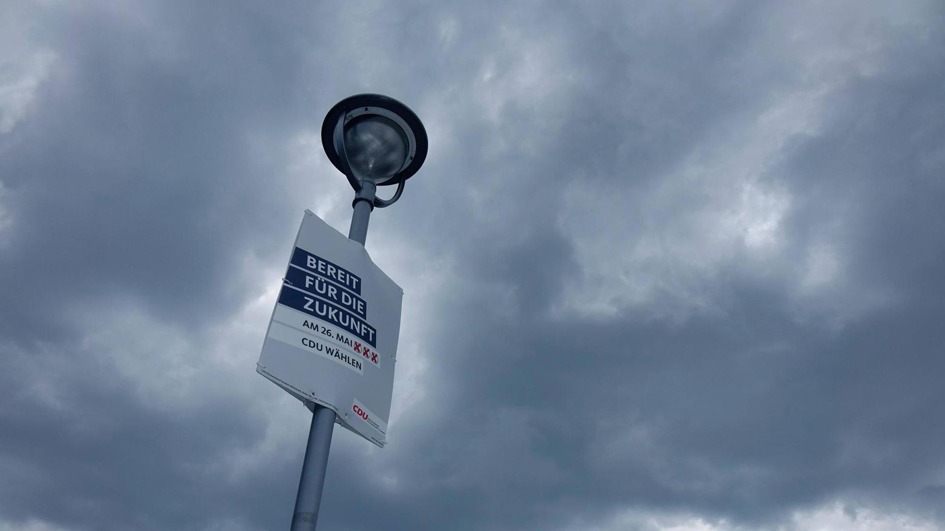Ein Wahlplakat der CDU an einem Laternenpfahl vor Himmel mit dunklen Wolken.