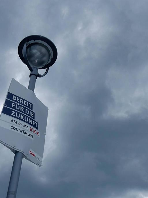 Ein Wahlplakat der CDU an einem Laternenpfahl vor Himmel mit dunklen Wolken.