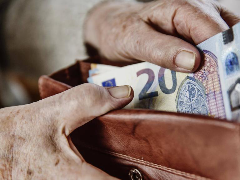 Eine Seniorin zieht einen 20 Euro Schein aus ihrem Portemonnaie.