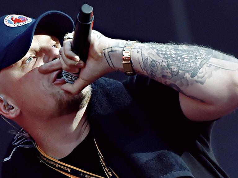 Der Hamburger Rapper Bonez MC steht auf einer Bühne und singt, er hält in der linken Hand ein Mikrofon.