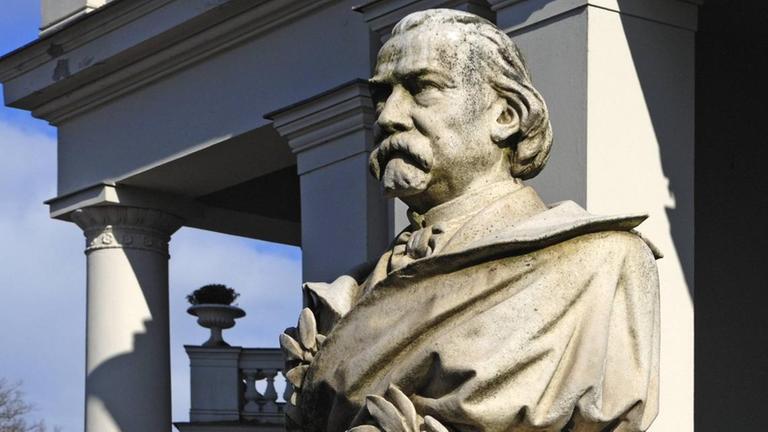 Ein Denkmal zeigt einen Mann mit großen Schnurrbart und halblangen Haaren.