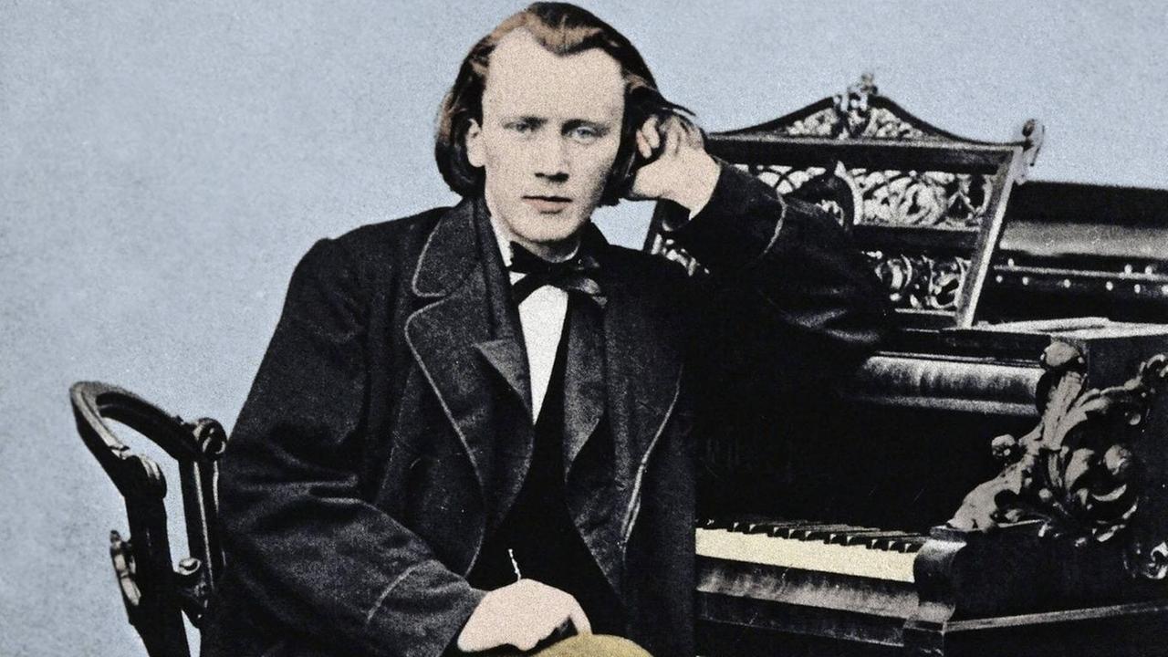 koloriertes Porträt des jungen Johannes Brahms (1833-1897), sitzend am Klavier, sich mit dem linken Arm aufstützend.