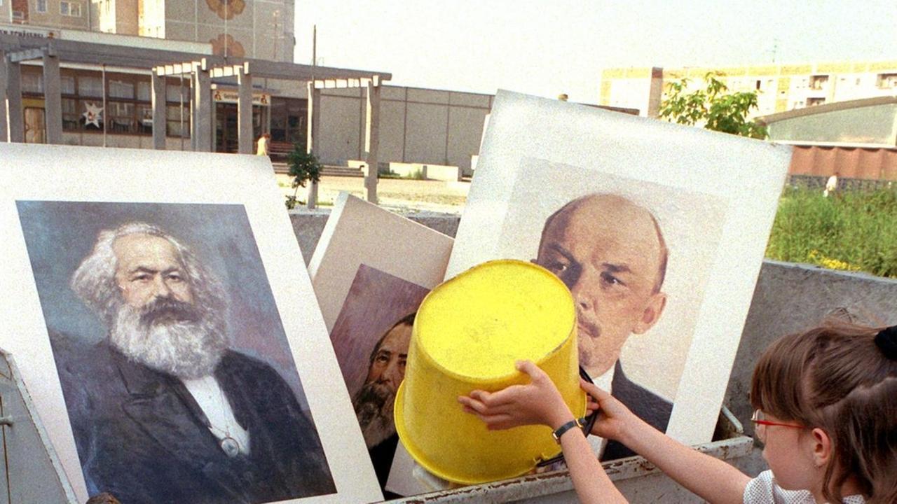 Ein Mädchen schüttet Abfall in einen Müllcontainer, in dem bereits die Bilder von Marx und Lenin liegen. Aufgenommen im Juli 1991 bei einer Aufräumaktion an einer Schule im Berliner Stadtbezirk Hellershof.
