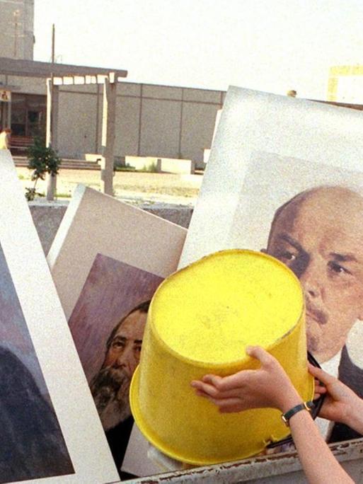 Ein Mädchen schüttet Abfall in einen Müllcontainer, in dem bereits die Bilder von Marx und Lenin liegen. Aufgenommen im Juli 1991 bei einer Aufräumaktion an einer Schule im Berliner Stadtbezirk Hellershof.