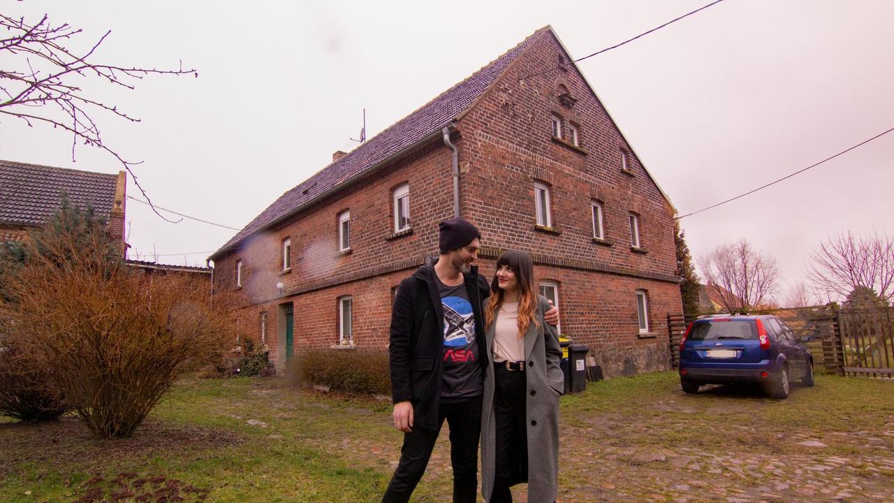 Ein Paar steht vor vor einem alten Bauernhaus.