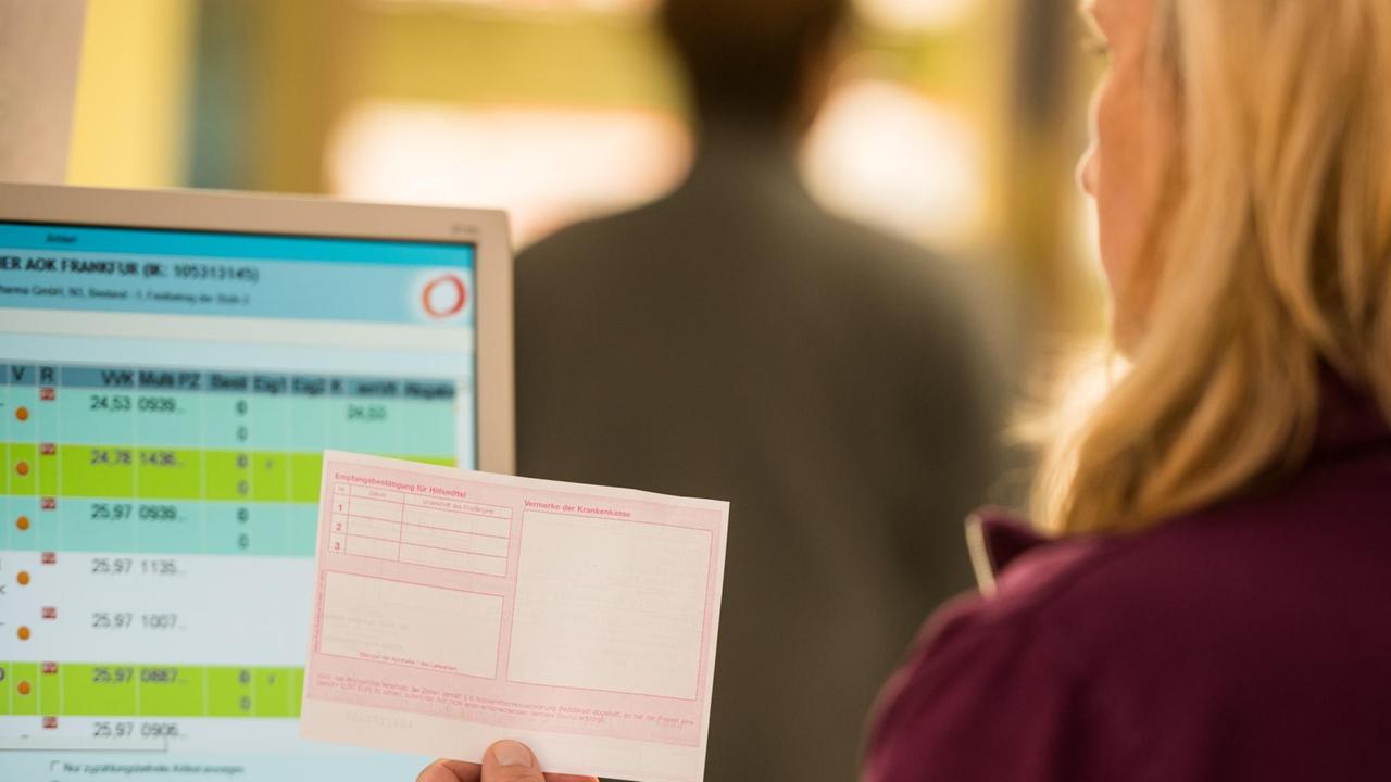 Apothekerin steht mit einem Rezept vor einem Computerbildschirm, Symbolbild Lieferengpässe von Medikamenten
