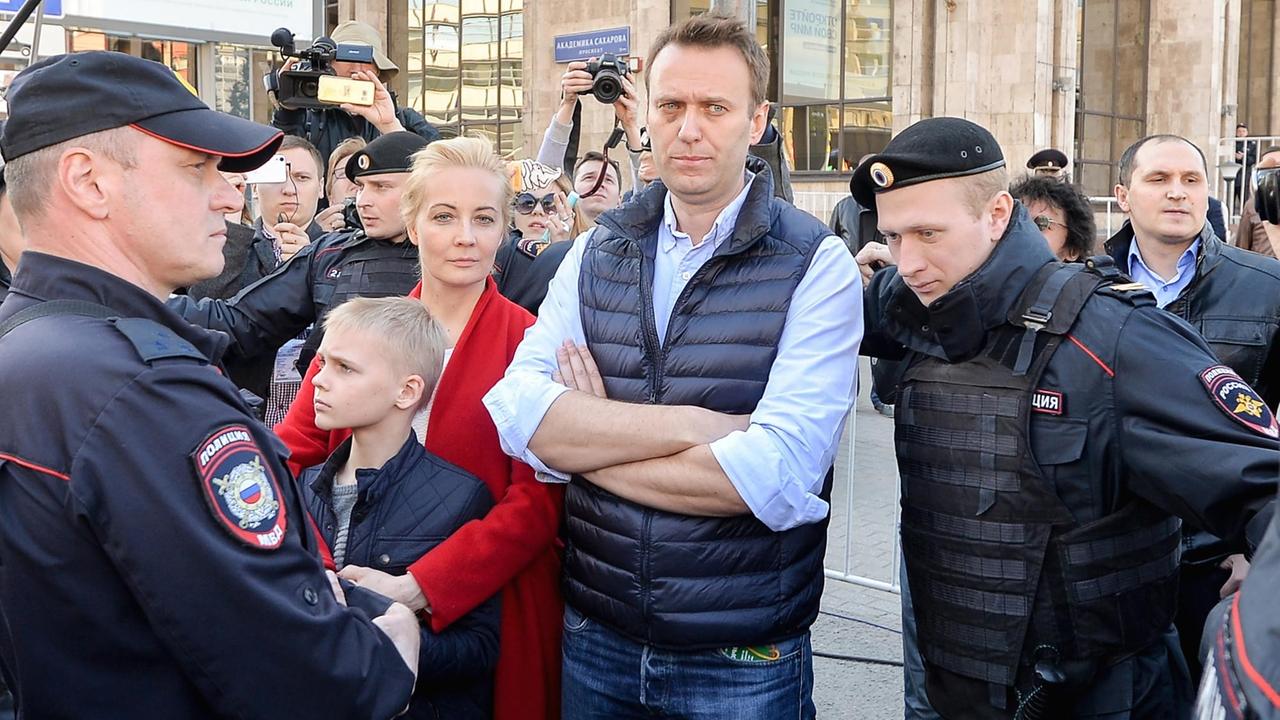 Alexej Nawalny steht mit verschränkten Armen neben seiner Frau Julia und seinem Sohn Zahar. Sie sind umringt von Polizisten.