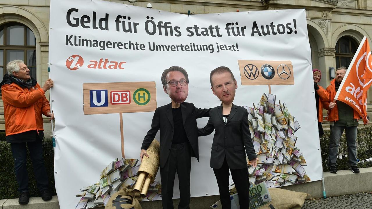 Zwei Aktivisten von attac stehen verkleidet als Bundesverkehrsminister Scheuer (l) und als VW-Vorstandsvorsitzender Diess vor dem Bundesverkehrsministerium.
