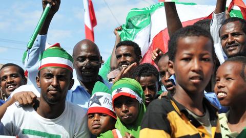 Schwarze Männer und Kinder in rot-weiß-grünen Flaggen und Kleidung feiern unter freiem Himmel.