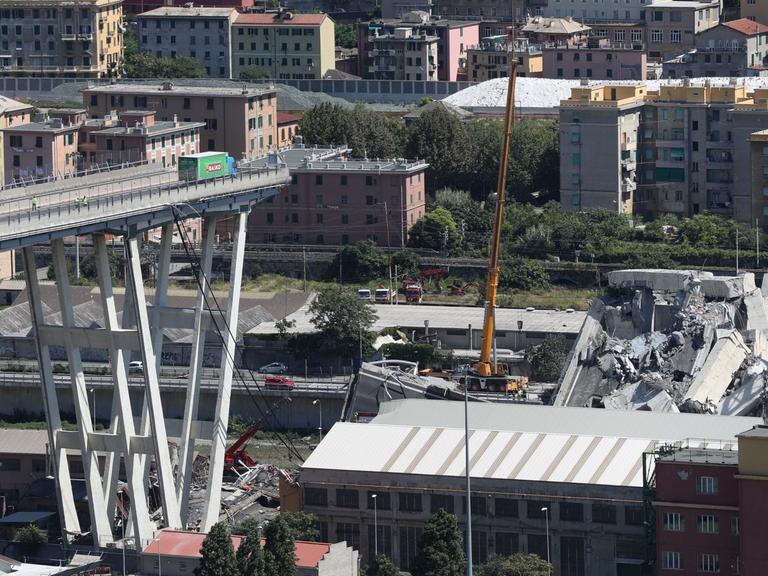 Mit Baggern und Kränen werden Trümmerteile der teilweise eingestürzten Brücke in Genua weggeräumt.