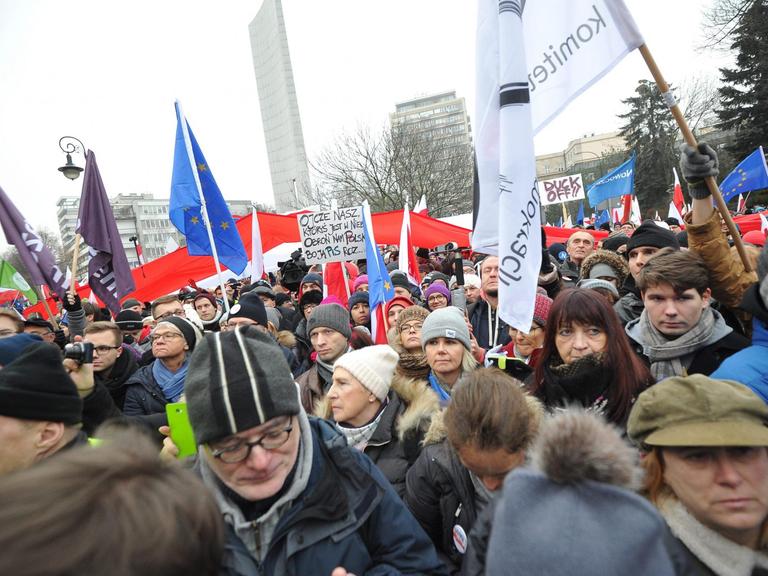 Eine Menschenmenge vor dem Parlamentsgebäude in Warschau hält Banner und Fahnen in die Höhe.