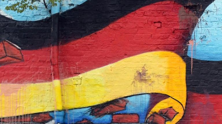 Passanten stehen in Berlin vor einem Wandbild mit der deutschen Nationalflagge.