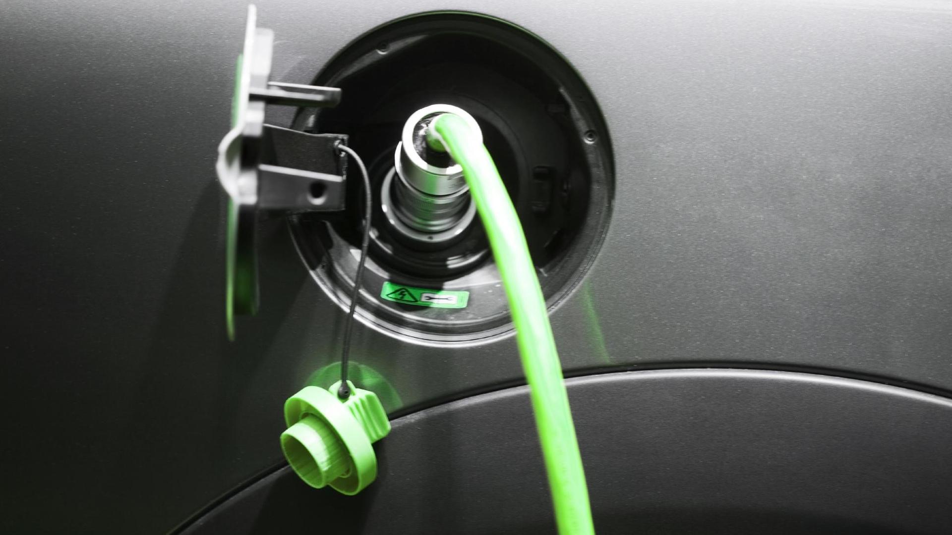 Ein grüner Stecker im "Tank" eines Elektroautos, das aufgeladen wird.