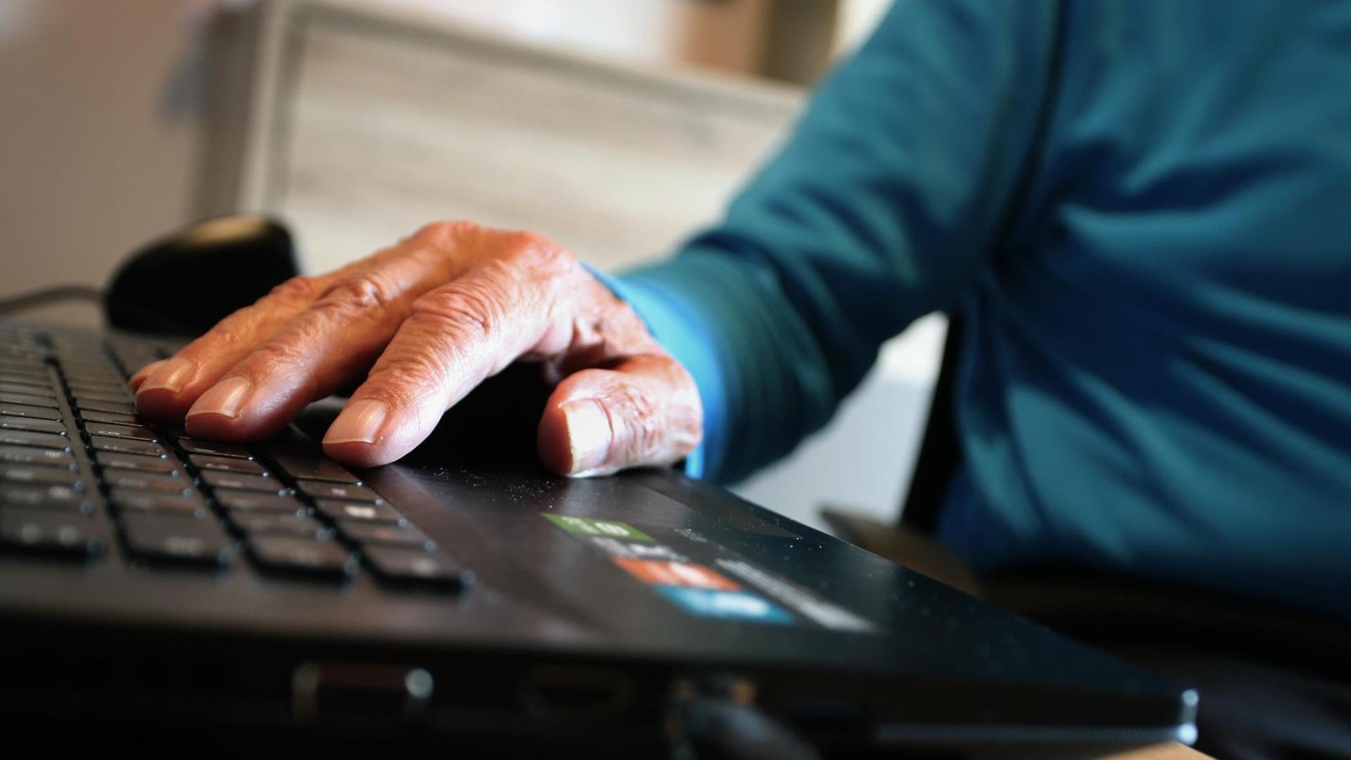 Die Hand eines alten Mannes liegt auf einer Computer-Tastatur
