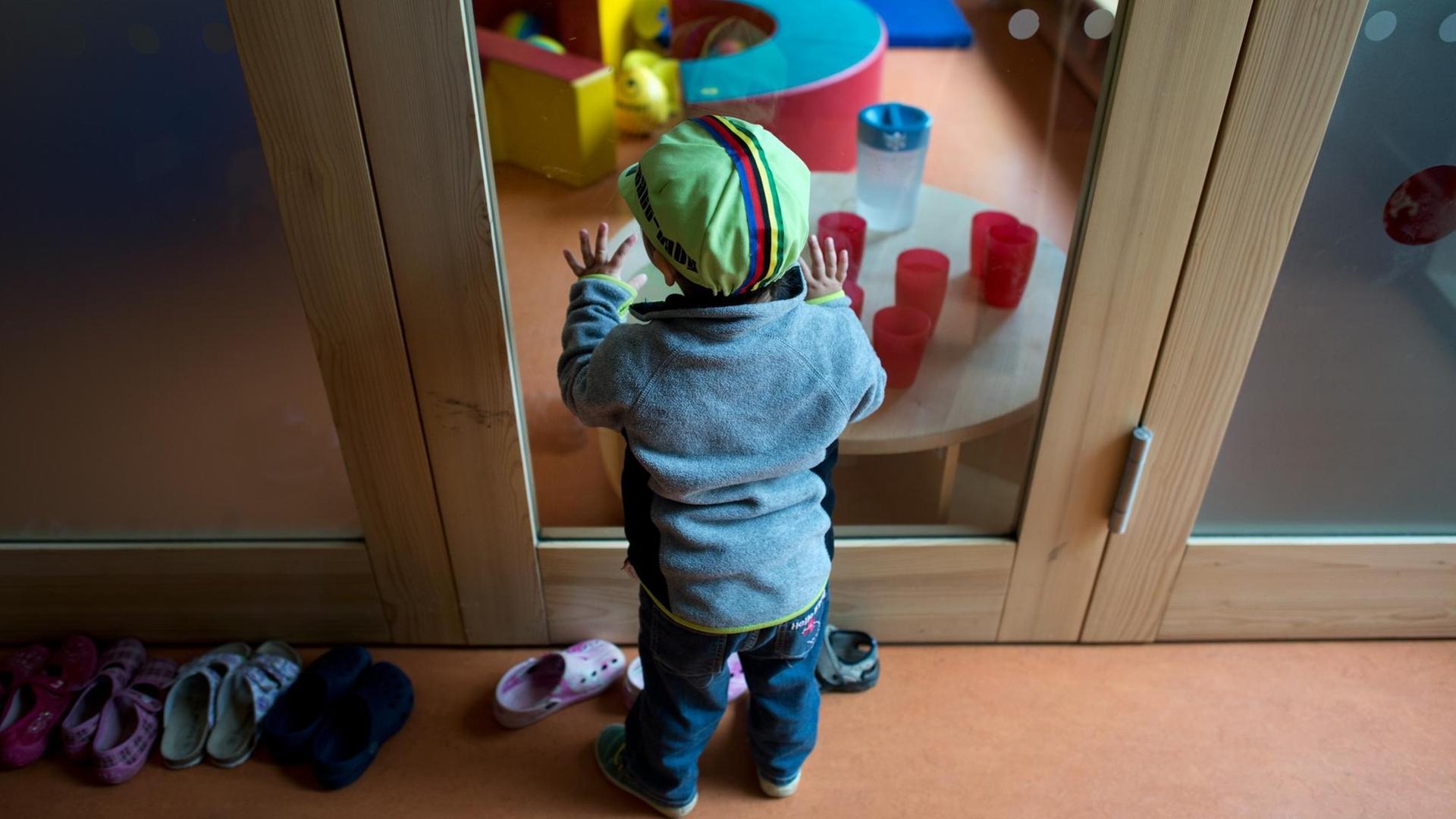 Ein Kleinkind steht an einer Glasscheibe in einer Kindertagesstätte.