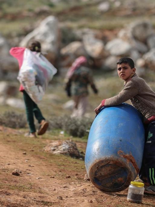 Ein syrischer Junge hält ein Plastikfass, im Hintergrund laufen Kinder mit Plastiksäcken.