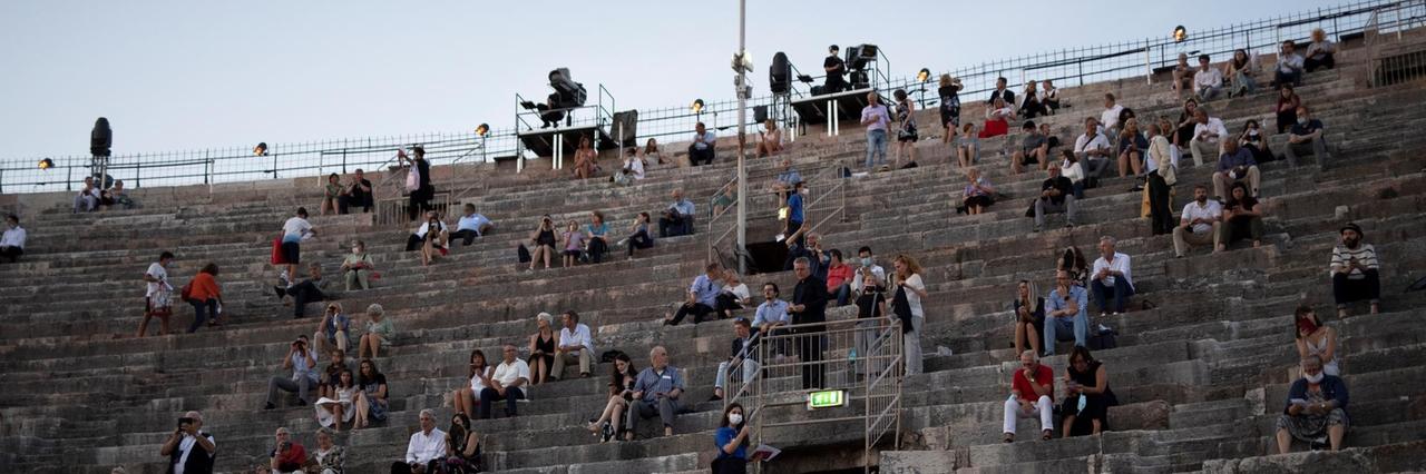 Zuschauerinnen und Zuschauer sitzen mit coronabedingtem Abstand auf den Steinstufen der Arena 