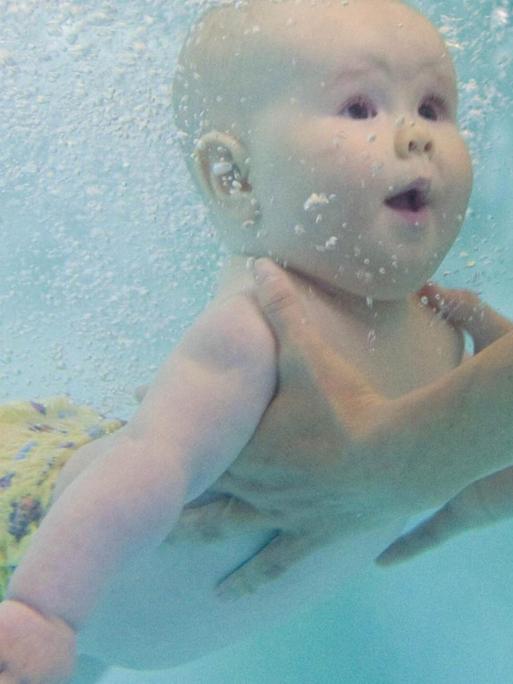 Die Unterwasseraufnahme eines Babys, das beim Schwimmunterricht unter Wasser festgehalten wird