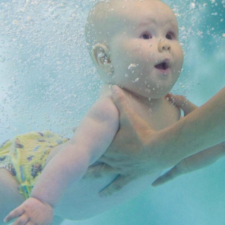 Die Unterwasseraufnahme eines Babys, das beim Schwimmunterricht unter Wasser festgehalten wird 