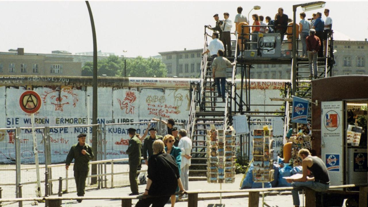 Aussichtsplattform mit Besuchern am Potsdamer Platz in West-Berlin. Links stehen Grenzbeamte hinter Absperrgittern. Aufnahme von 1988. 