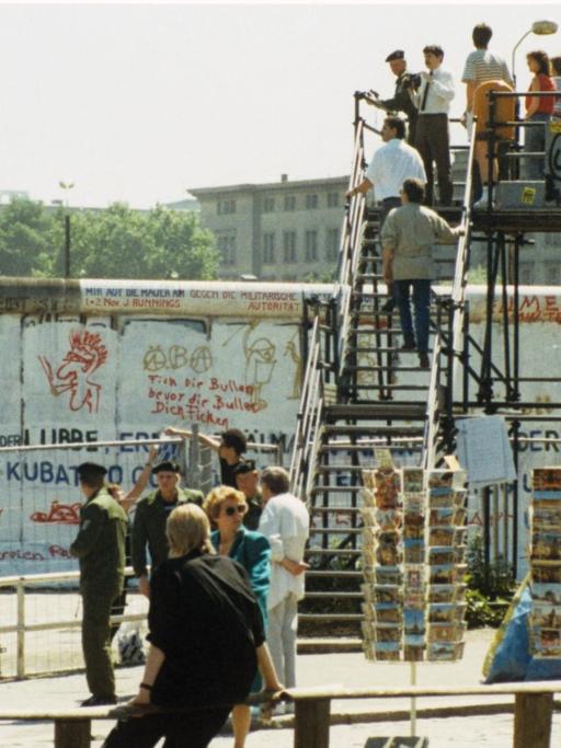 Aussichtsplattform mit Besuchern am Potsdamer Platz in West-Berlin. Links stehen Grenzbeamte hinter Absperrgittern. Aufnahme von 1988.