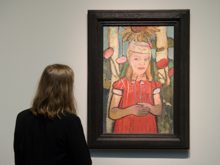 Eine Frau betrachtet das Werk "Mädchen in rotem Kleid vor Sonnenblume" (1907) von Paula Modersohn-Becker im Bucerius Kunstforum in Hamburg.