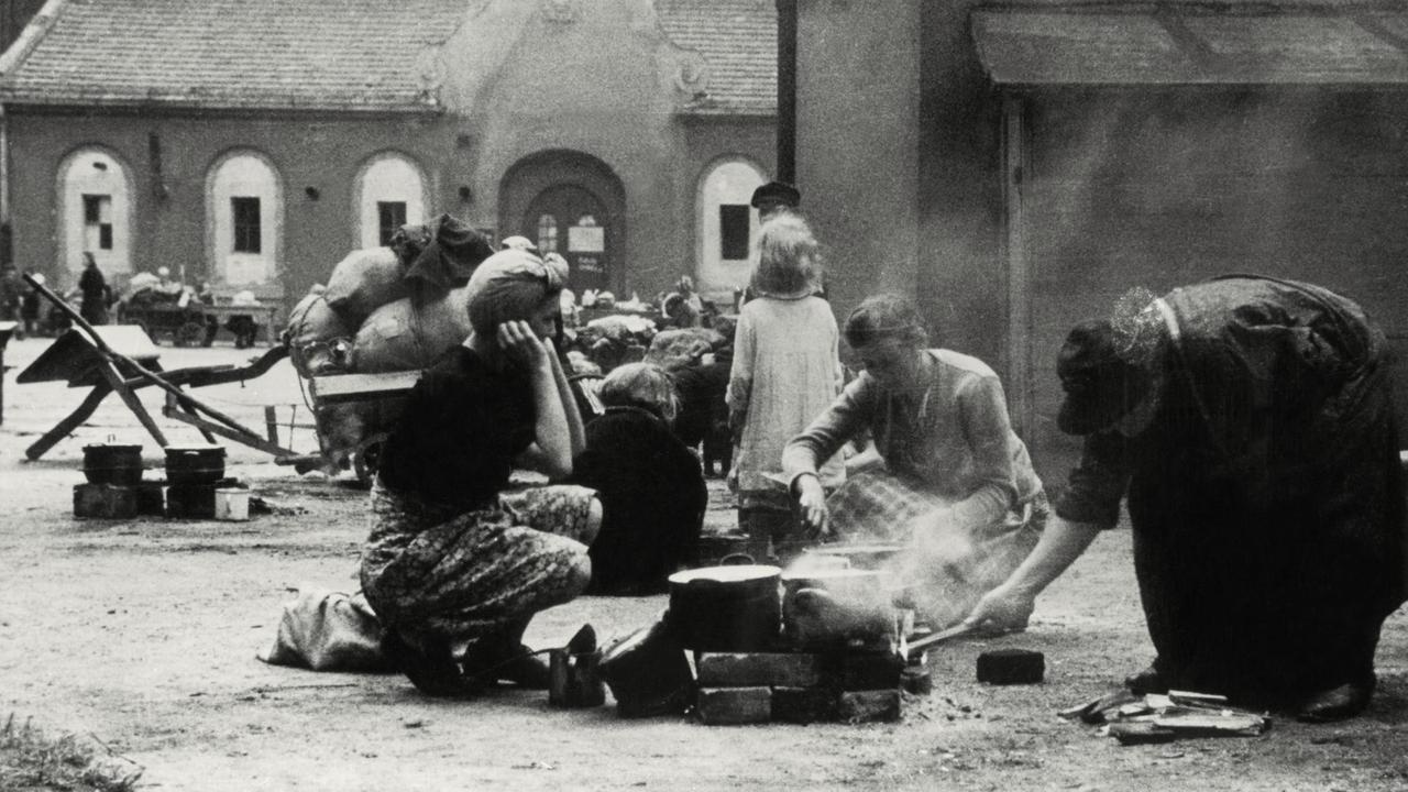 Frauen beim Kochen an einer offenen Feuerstelle in einem Flüchtlingskamp in Berlin, Juli 1945.