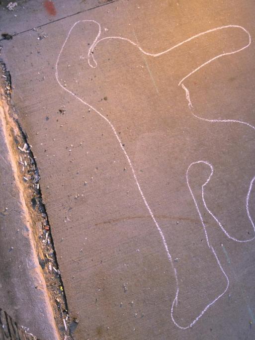 Im schummrigen Licht einer Straßenlaterne ist ein mit Kreide gezeichneter Umriss eines Menschen zu erkennen.