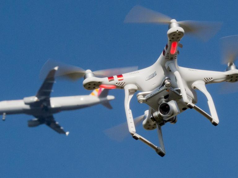 Das Foto zeigt eine private Drohne, dahinter in weiter Entfernung ein Flugzeug im Anflug auf den Flughafen Düsseldorf.