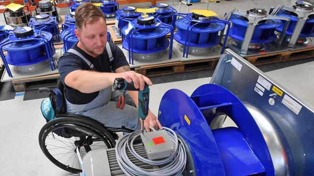 An einem Arbeitsplatz für Motor-Klemmen ist ein Mann im Roll-Stuhl mit Arbeiten beschäftigt.
