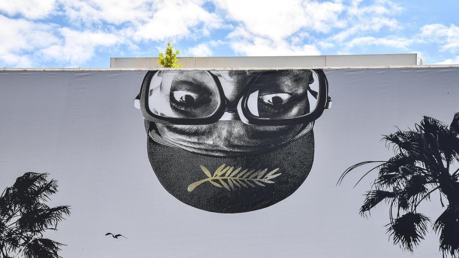 Ein riesiges Banner der 74. Filmfestspiele von Cannes, mit der Darstellung eines umgedrehten, männlichen Kopfes mit Brille und dem Logo der Filmfestspiele.