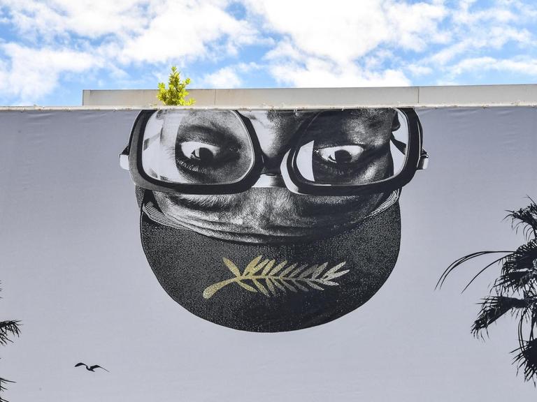 Ein riesiges Banner der 74. Filmfestspiele von Cannes, mit der Darstellung eines umgedrehten, männlichen Kopfes mit Brille und dem Logo der Filmfestspiele.