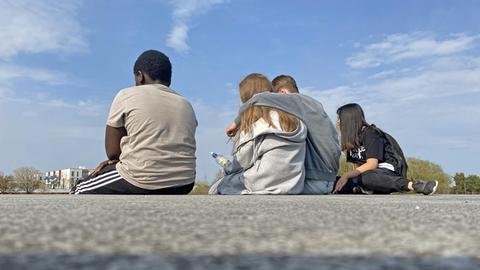 Vier Jugendliche sitzen auf einer Mauer im Riemer Park in München.