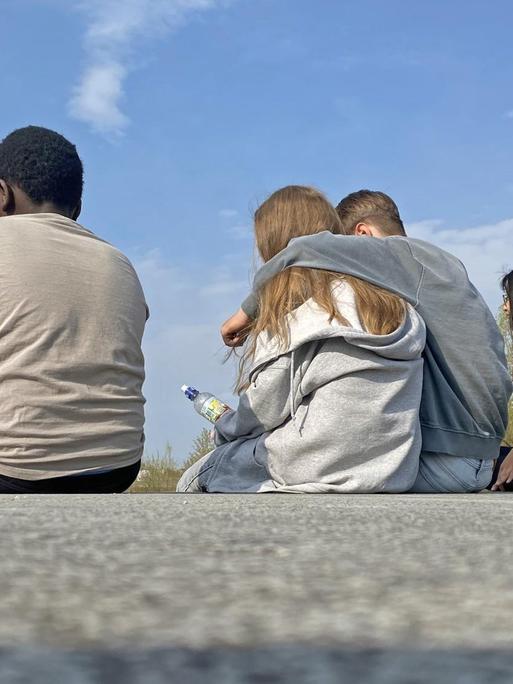 Vier Jugendliche sitzen auf einer Mauer im Riemer Park in München.