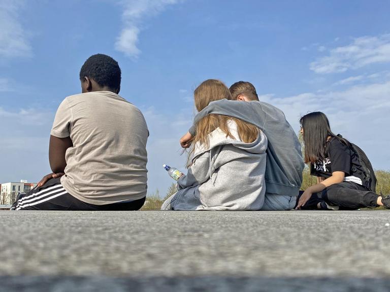 Vier Jugendliche sitzen auf einer Mauer im Riemer Park in München.