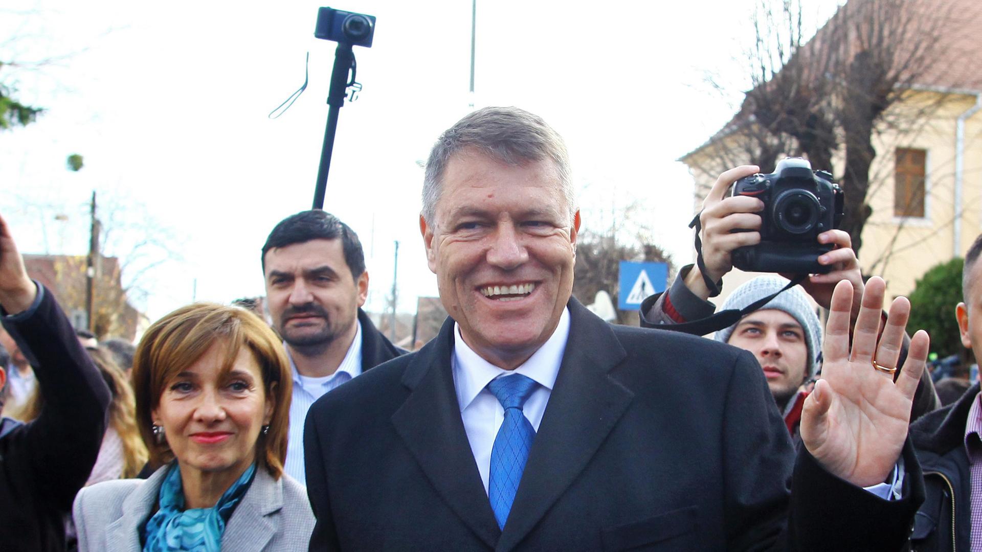 Der siegreiche Präsidentschaftskandidat Klaus Johannis verlässt mit seiner Frau ein Wahllokal und ist dabei umringt von Fotografen.