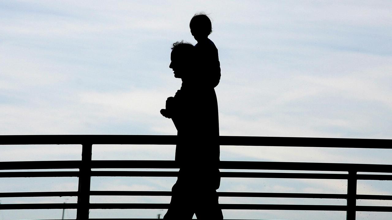 Ein Mann trägt bei einem Spaziergang über eine Brücke ein Kleinkind auf seinen Schultern