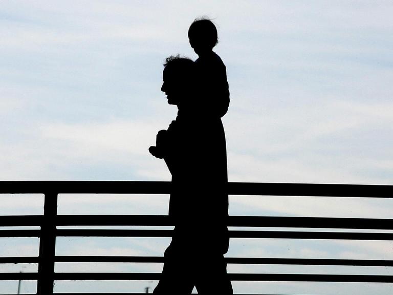 Ein Mann trägt bei einem Spaziergang über eine Brücke ein Kleinkind auf seinen Schultern