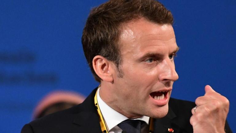 Macron steht mit der Karlspreismedaille am Rednerpult und ballt die Faust.